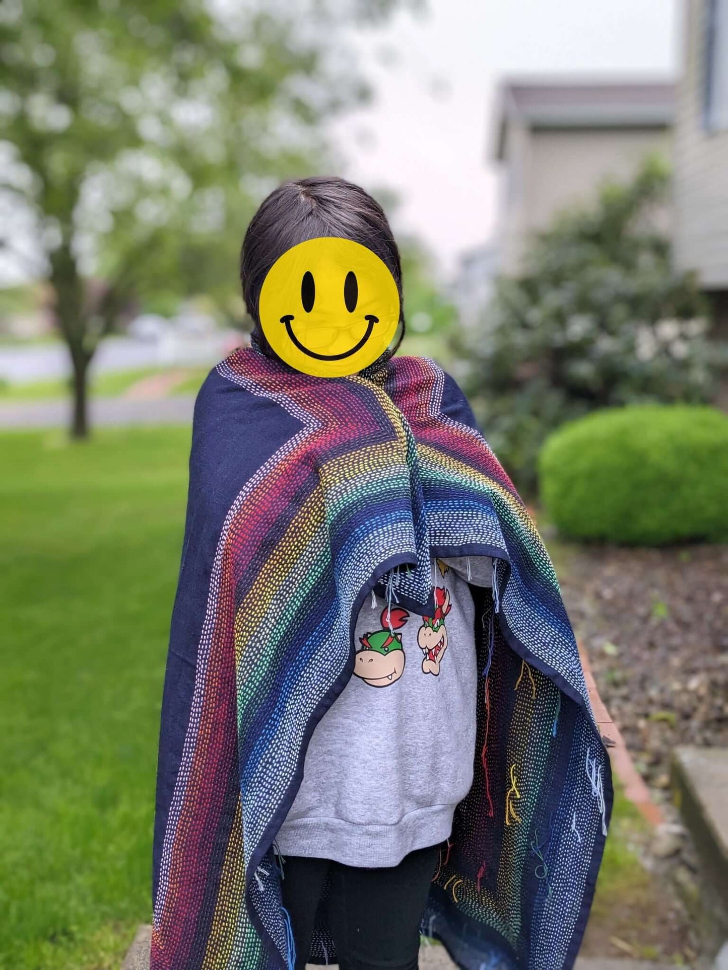 Person wrapped in a colorful sashiko fabric standing outdoors with a smiley face mask