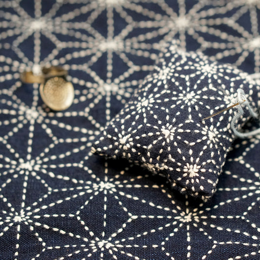 Sashiko stitching pattern on blue fabric with needle and thimble for Japanese mending and sustainable sewing workshops in 2024/2025